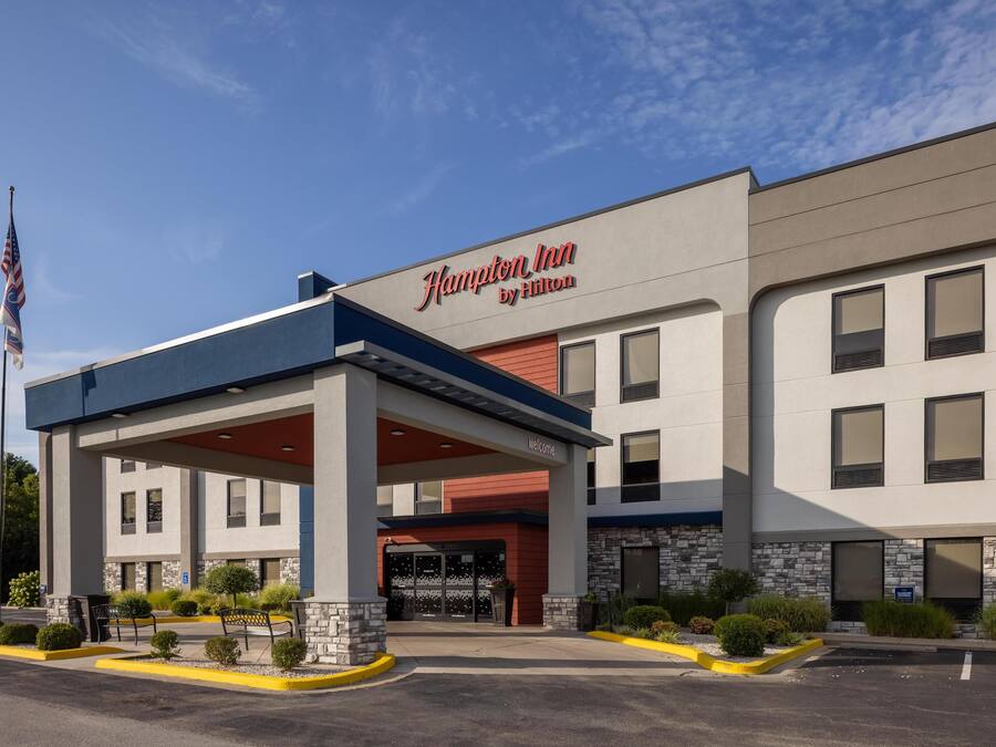 Edificio de un Hampton Inn by Hilton con vestíbulo cubierto, fachada de piedra y una bandera.