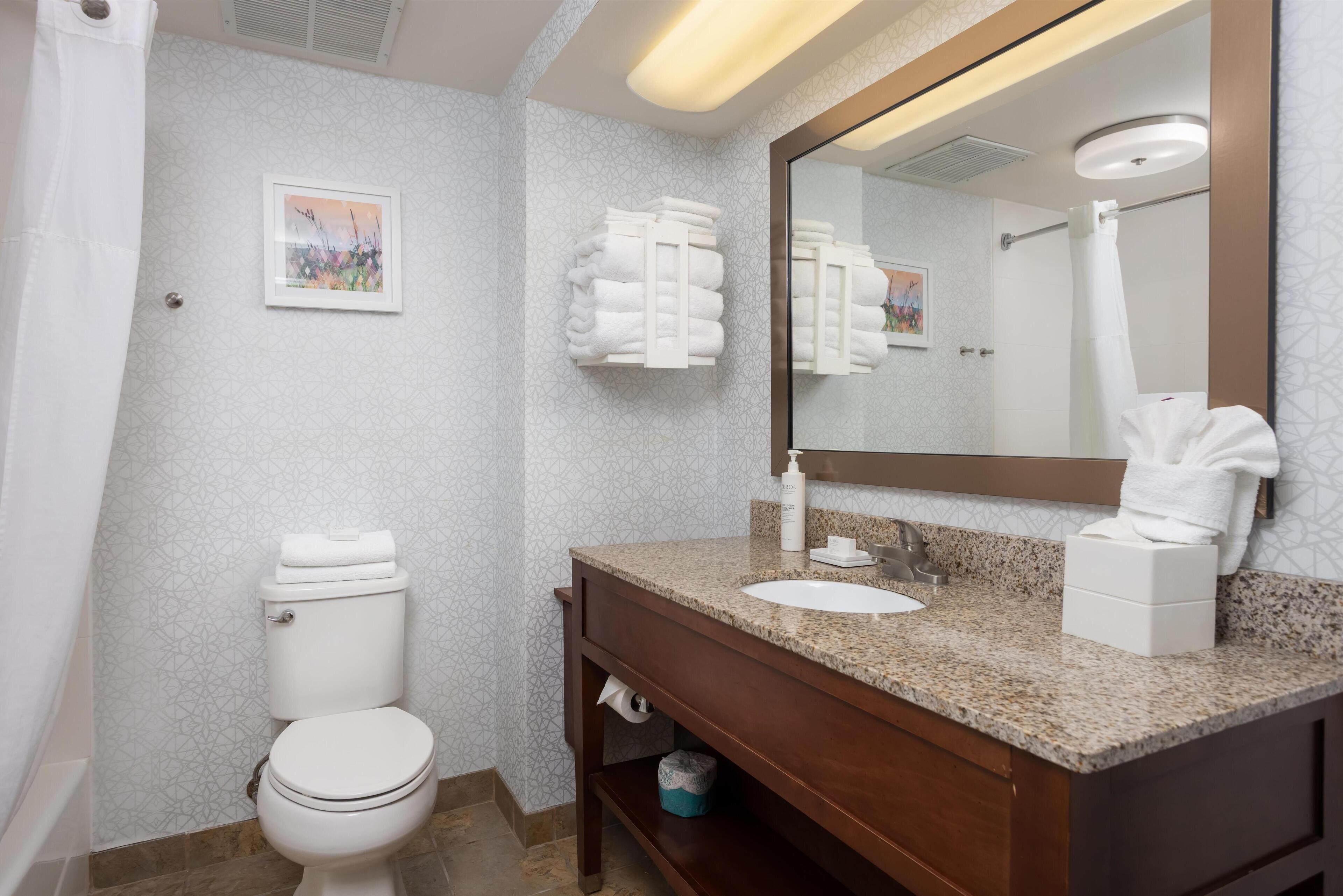 A bathroom with a toilet, sink, and mirror. There are towels and a picture on the wall.