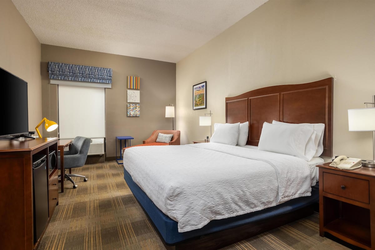 A hotel room with a large bed, a desk with a computer, a chair, and a television.
