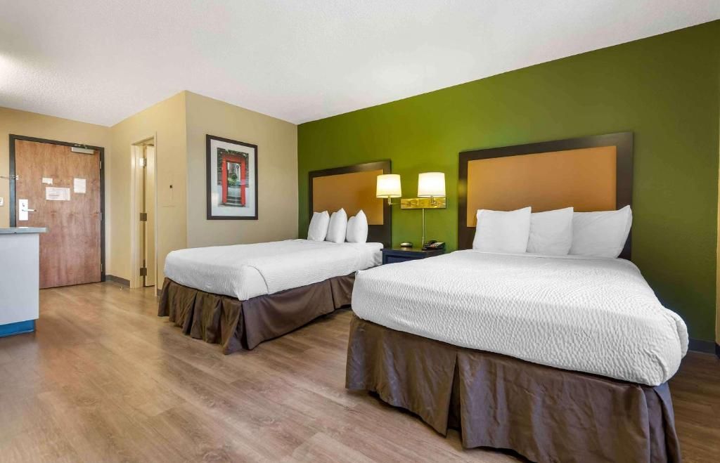 Une chambre d’hôtel avec deux lits, un bureau et un mur d’accent vert.