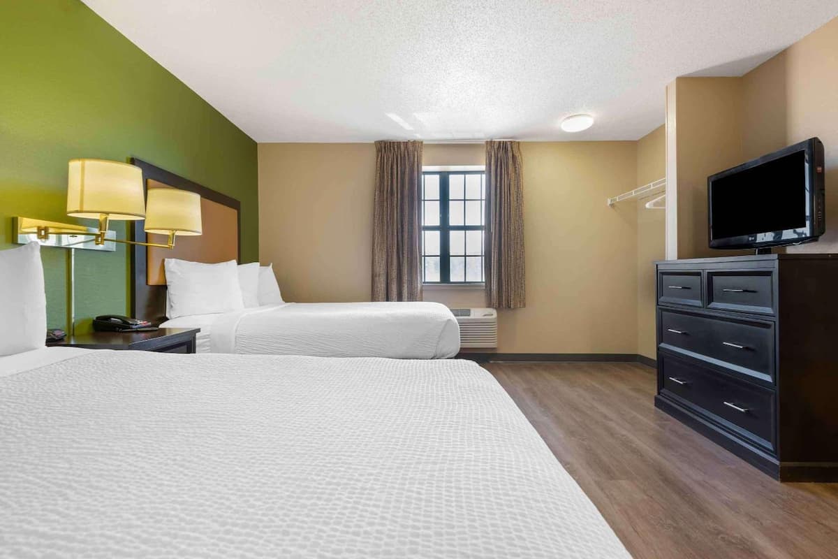 A hotel room with two beds, a TV, a dresser, and a window with curtains.