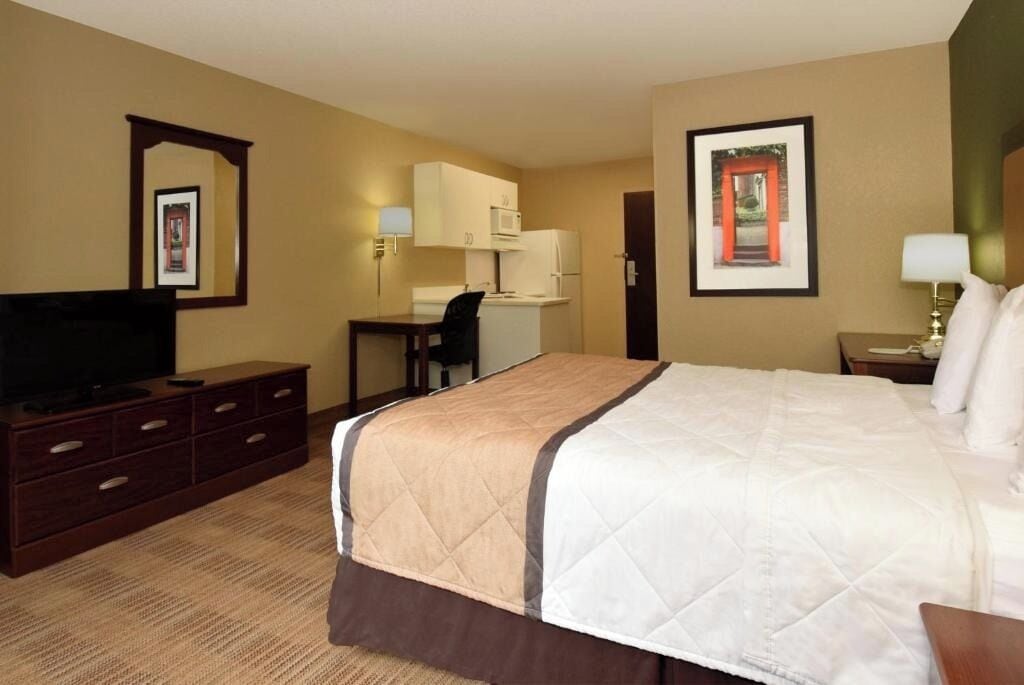 A hotel room with a bed, a desk, a television, and a picture on the wall.