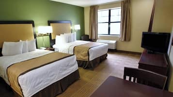 A hotel room with two beds, a desk, a chair, a television, and a window with curtains.