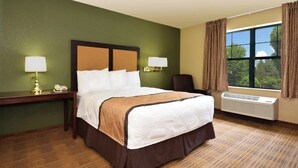 A hotel room with a large bed, two bedside lamps, a chair, a desk, and a window with curtains. - Studio 6 Corporate Extended Stay Buffalo Amherst NY (Buffalo)