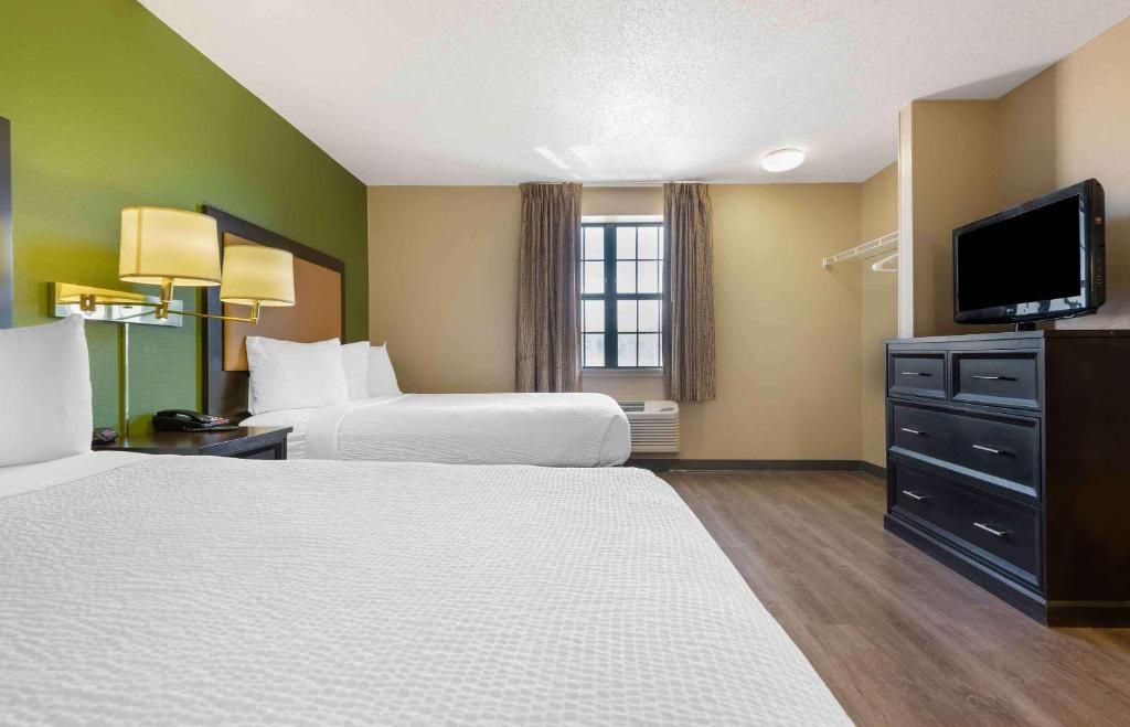 A hotel room with two beds, a television, a dresser, and a window with curtains.