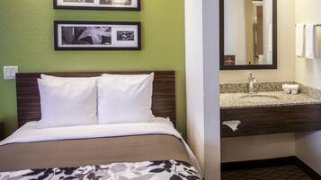 A hotel room with a bed, a bathroom with a sink and mirror, and two framed pictures on the wall.