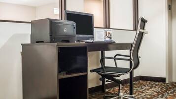 A hotel workspace with a desk, computer, printer, and a black office chair.