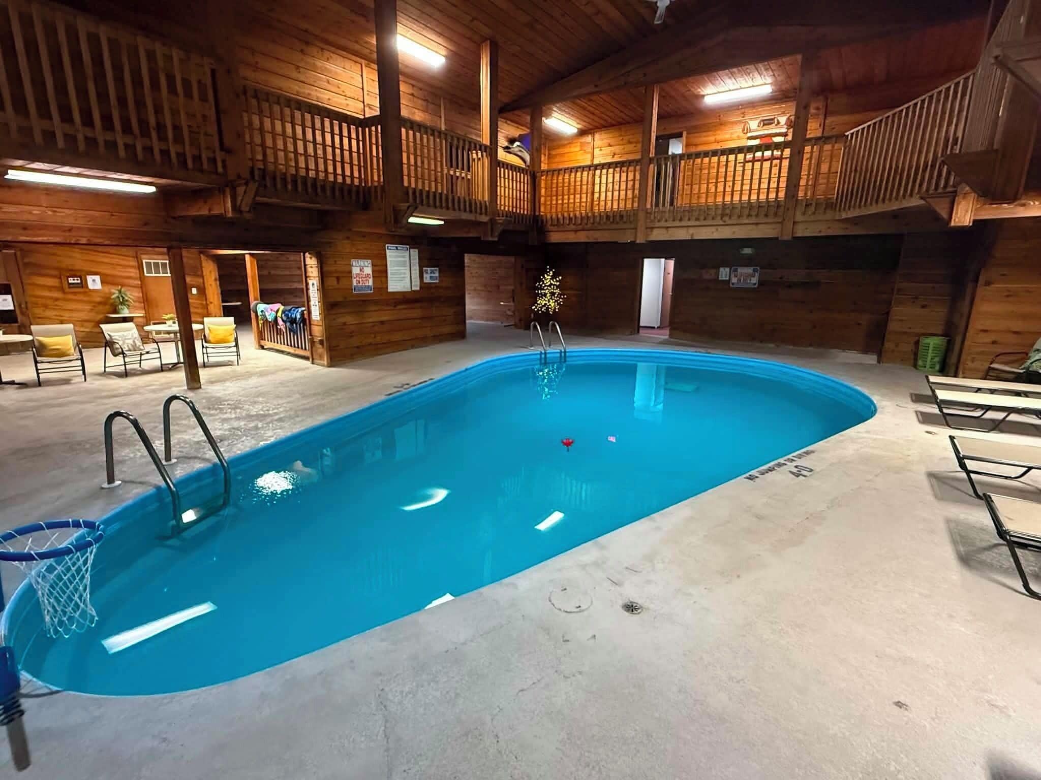 An indoor swimming pool with a wooden deck area, lounge chairs, and a lifeguard station.