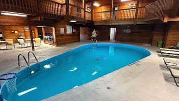 An indoor swimming pool with a wooden deck area, lounge chairs, and a lifeguard station.