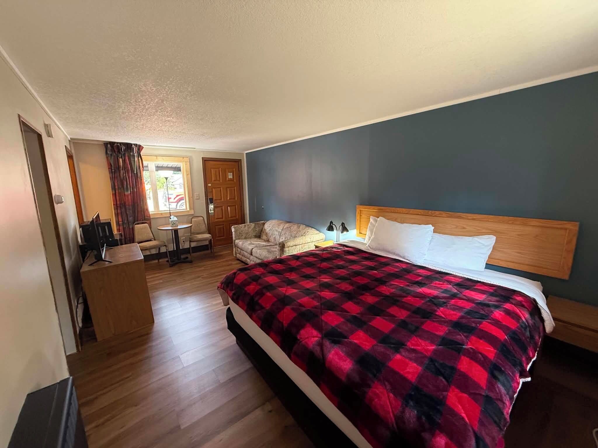 A hotel room with a bed, a desk, a chair, and a small table.