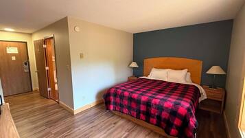 A hotel room with a wooden floor, a bed with a red and black checkered bedspread, two bedside lamps, and a nightstand.