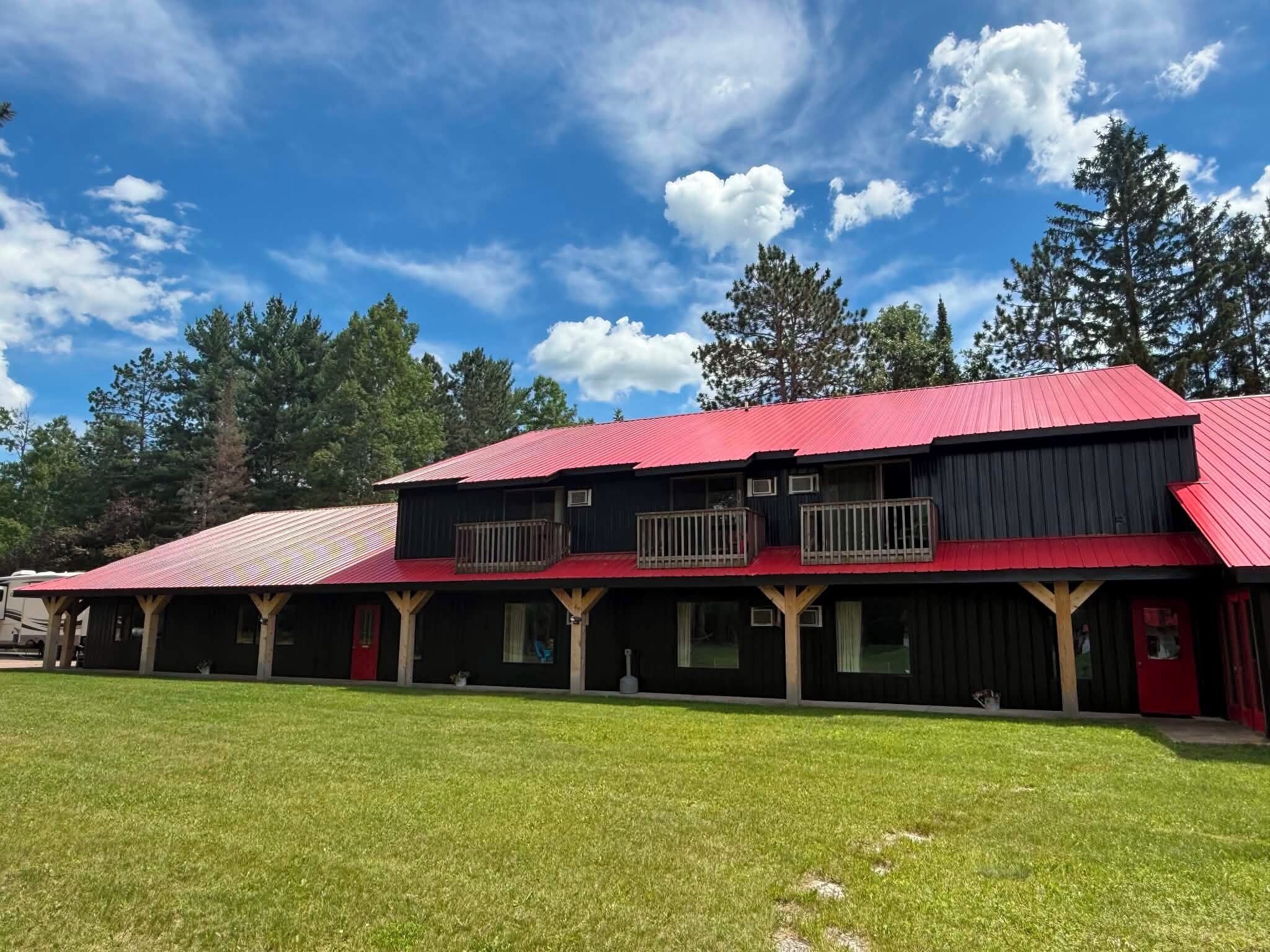 A two-story building with a red roof and black siding, featuring a covered porch with wooden posts and a red door.