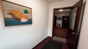 A hallway with a wooden duck painting, a dark mat at the entrance, and a door leading to a room with a plant and a small statue. - Northwestern Lodge (Hayward)