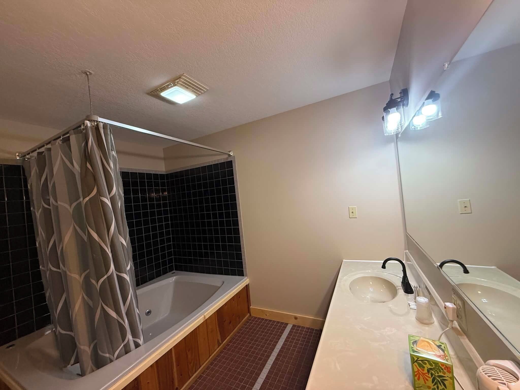 A bathroom with a bathtub, a shower curtain, a sink, and a mirror.