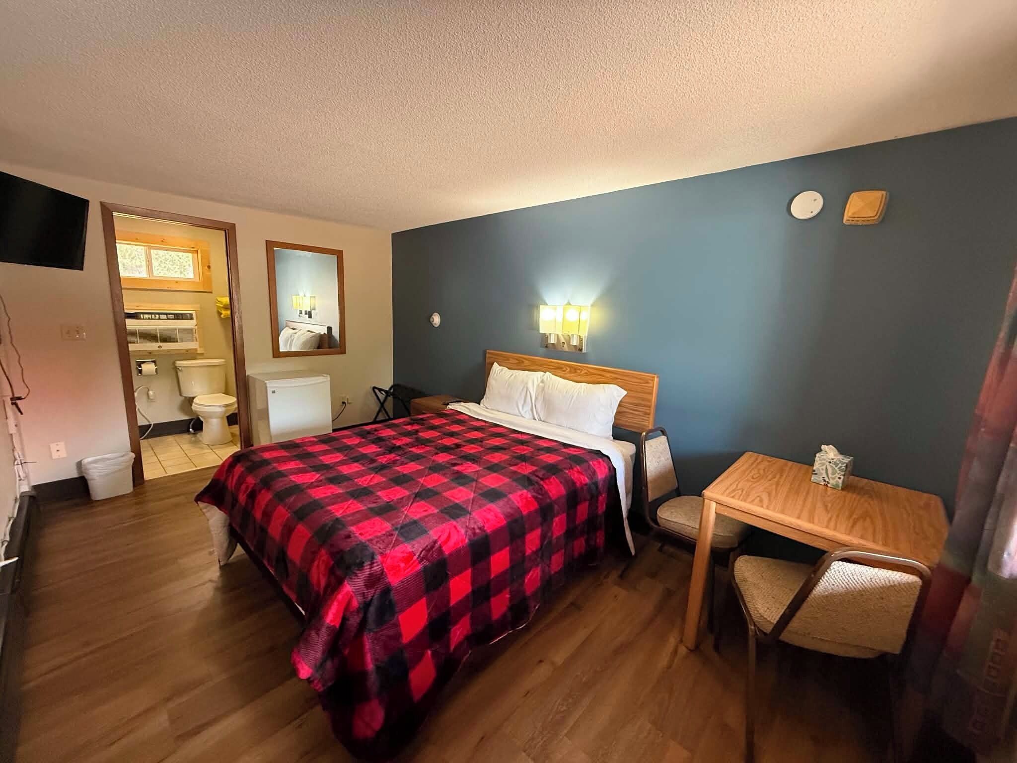 Een hotelkamer met een bed, een bureau, een stoel, een spiegel en een zichtbare badkamer door een geopende deur.