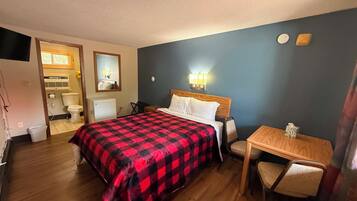 Een hotelkamer met een bed, een bureau, een stoel, een spiegel en een zichtbare badkamer door een geopende deur.