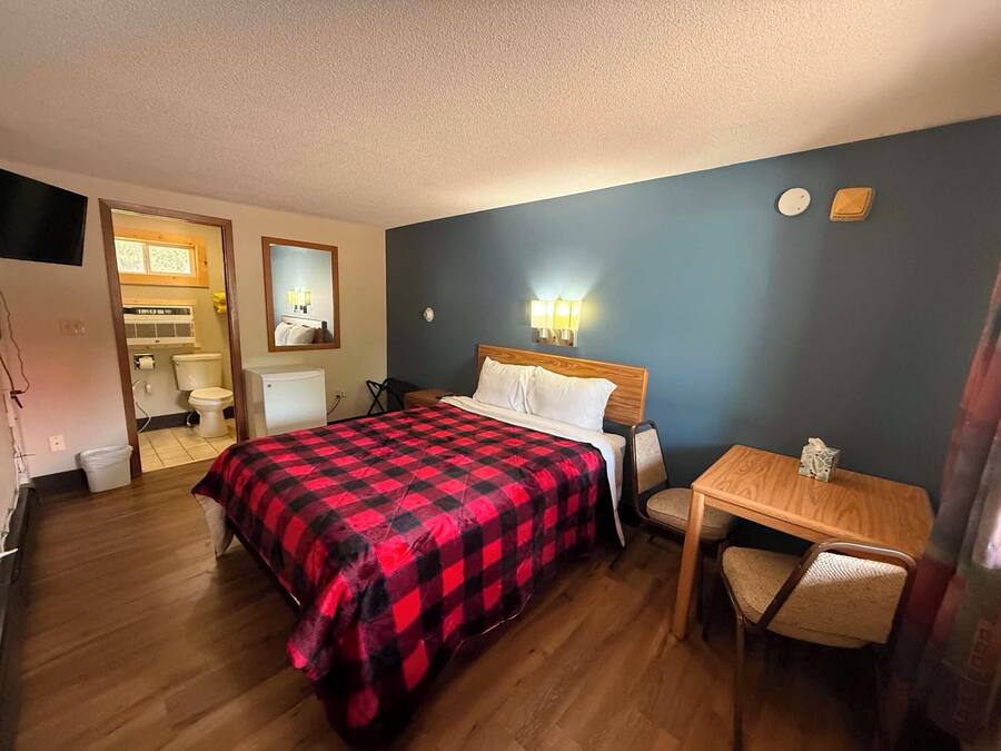 Een hotelkamer met een bed, een bureau, een stoel, een spiegel en een zichtbare badkamer door een geopende deur.