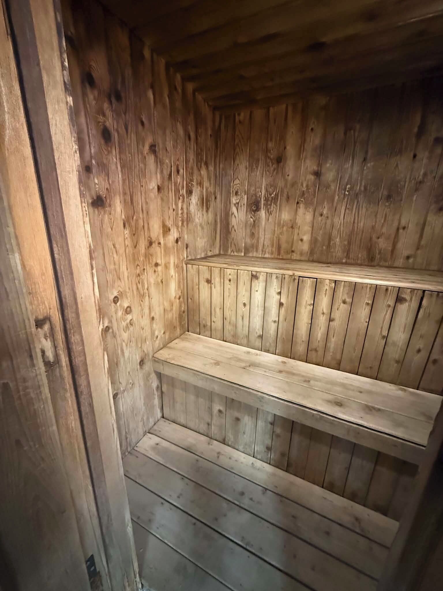 A wooden sauna with benches and a sloped floor.