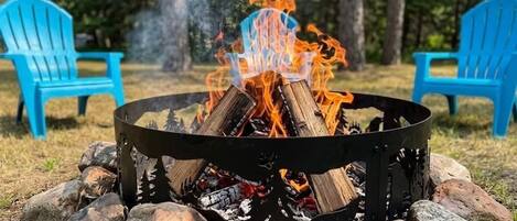 Ein Lagerfeuer mit Holzscheiten und Steinen, umgeben von blauen Stühlen in einer Freiluftumgebung.