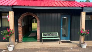 A building with a red roof, a brick archway entrance, a bench, and potted plants. - Northwestern Lodge (Hayward)