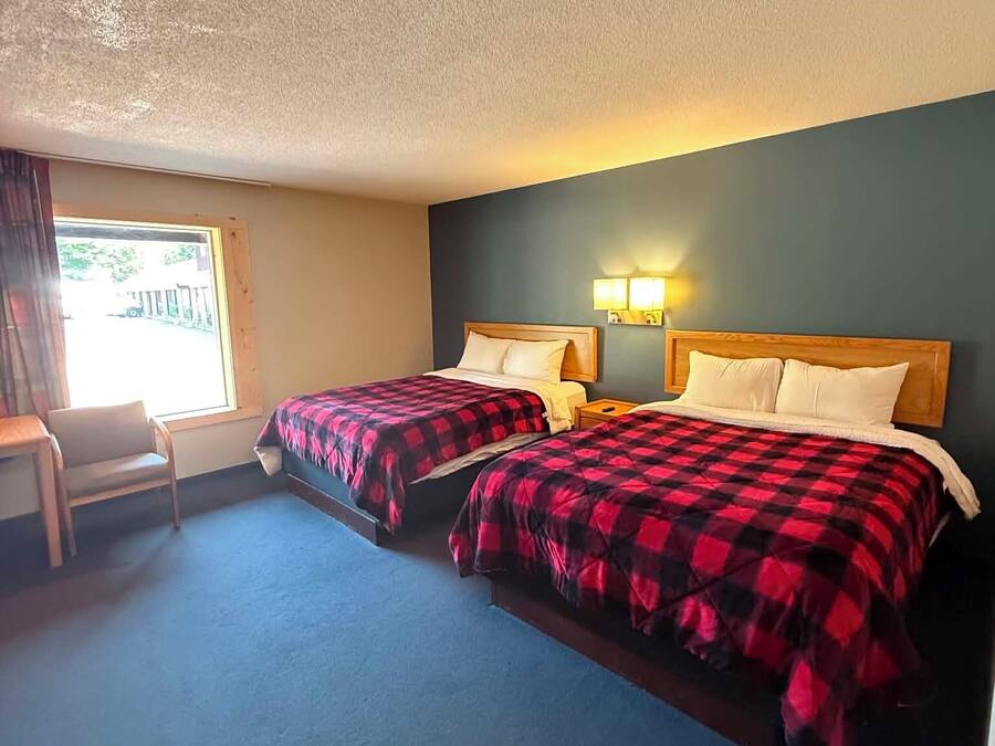 A hotel room with two beds, a chair, and a window.