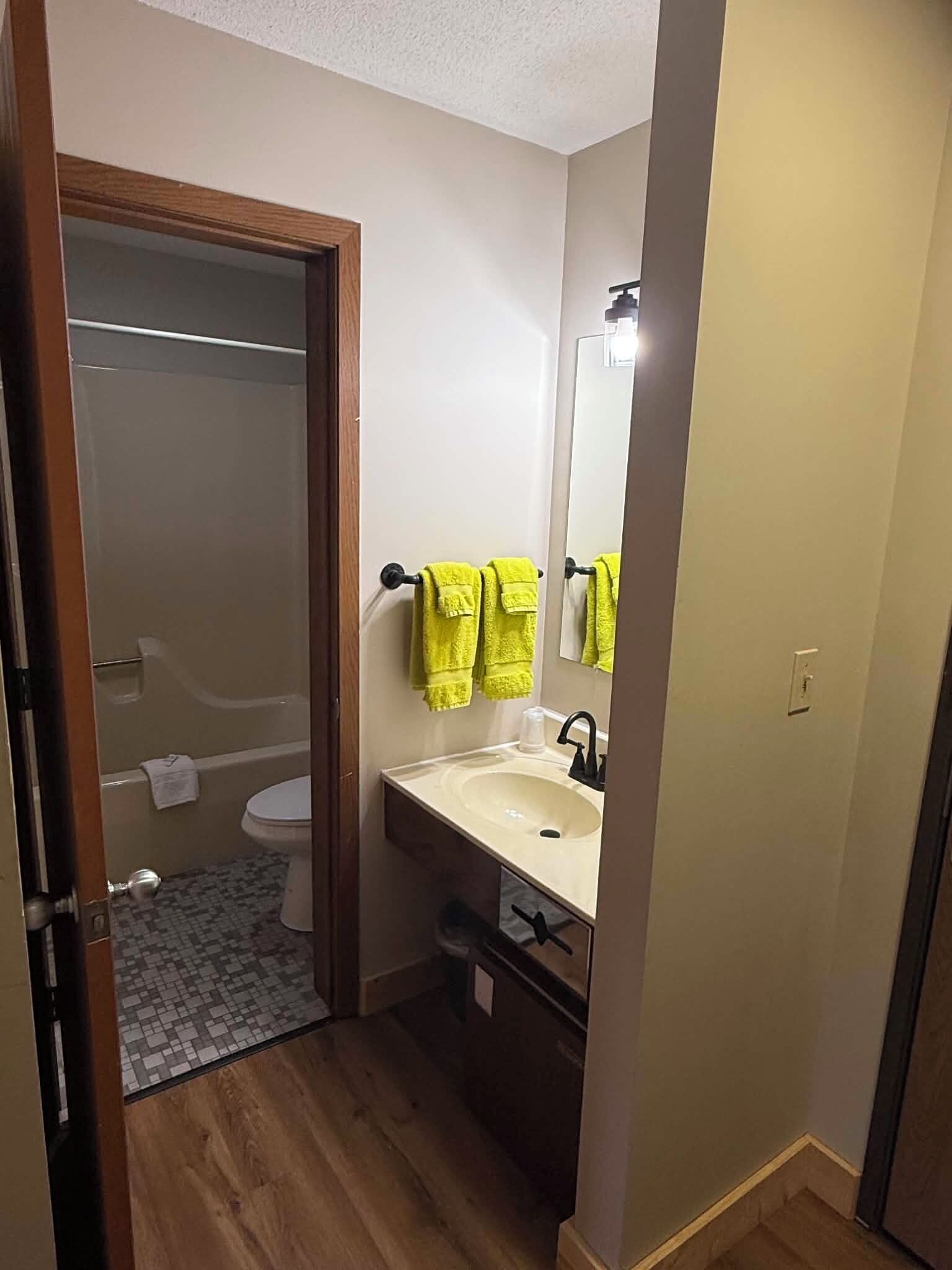 A bathroom with a toilet, sink, mirror, and yellow towels.