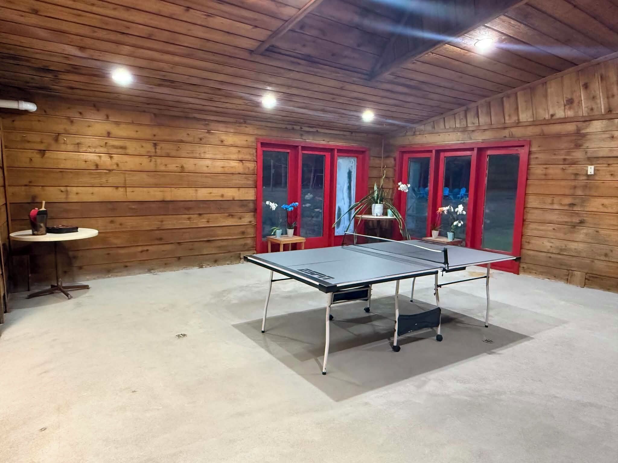 A ping pong table in a room with wooden walls and red-framed windows.
