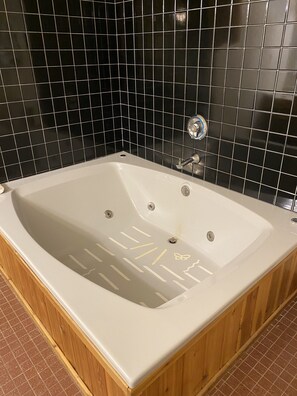 A rectangular bathtub with a wooden frame, a faucet, and a drain.