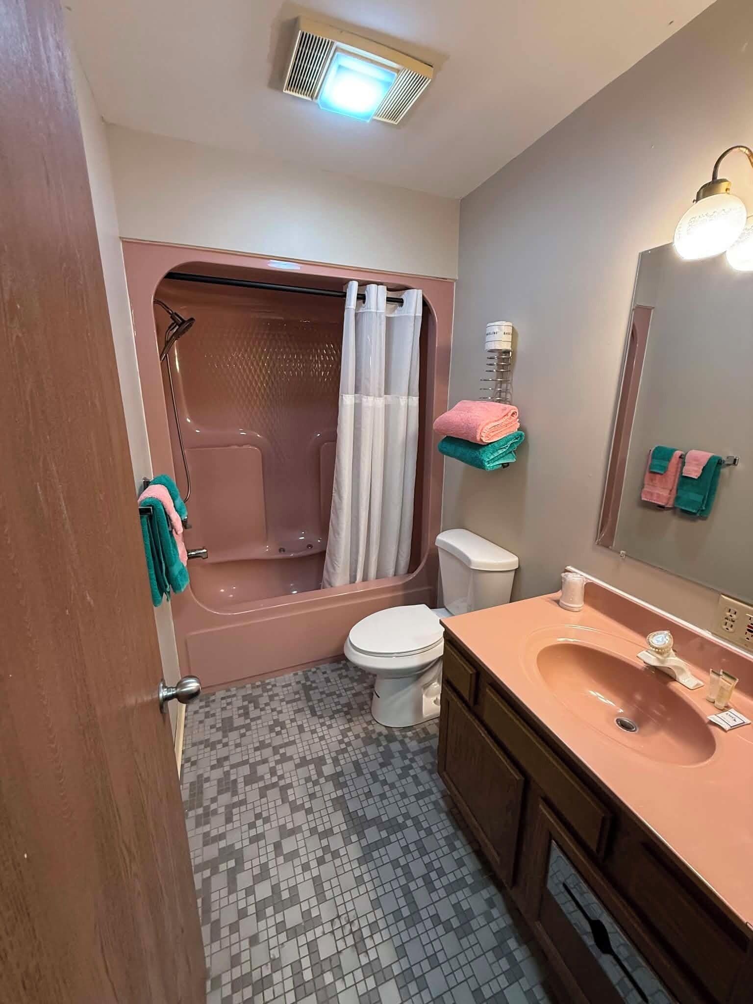 A bathroom with a shower, toilet, sink, and a mirror with lights.