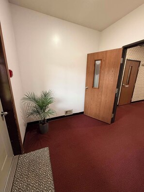A hallway with a red carpet, a wooden door, and a potted plant. - Northwestern Lodge (Hayward)
