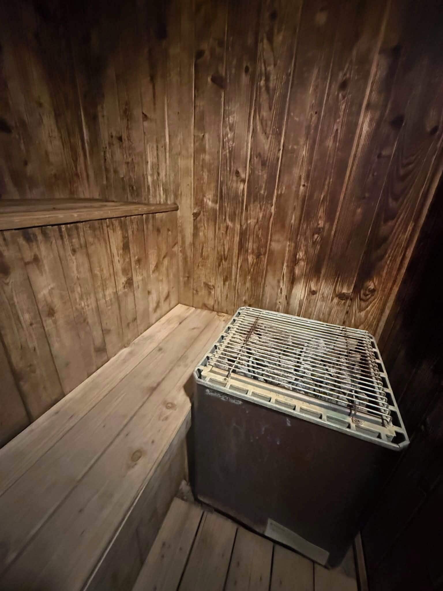 Interior de una cabaña de madera con un banco y un armario metálico.