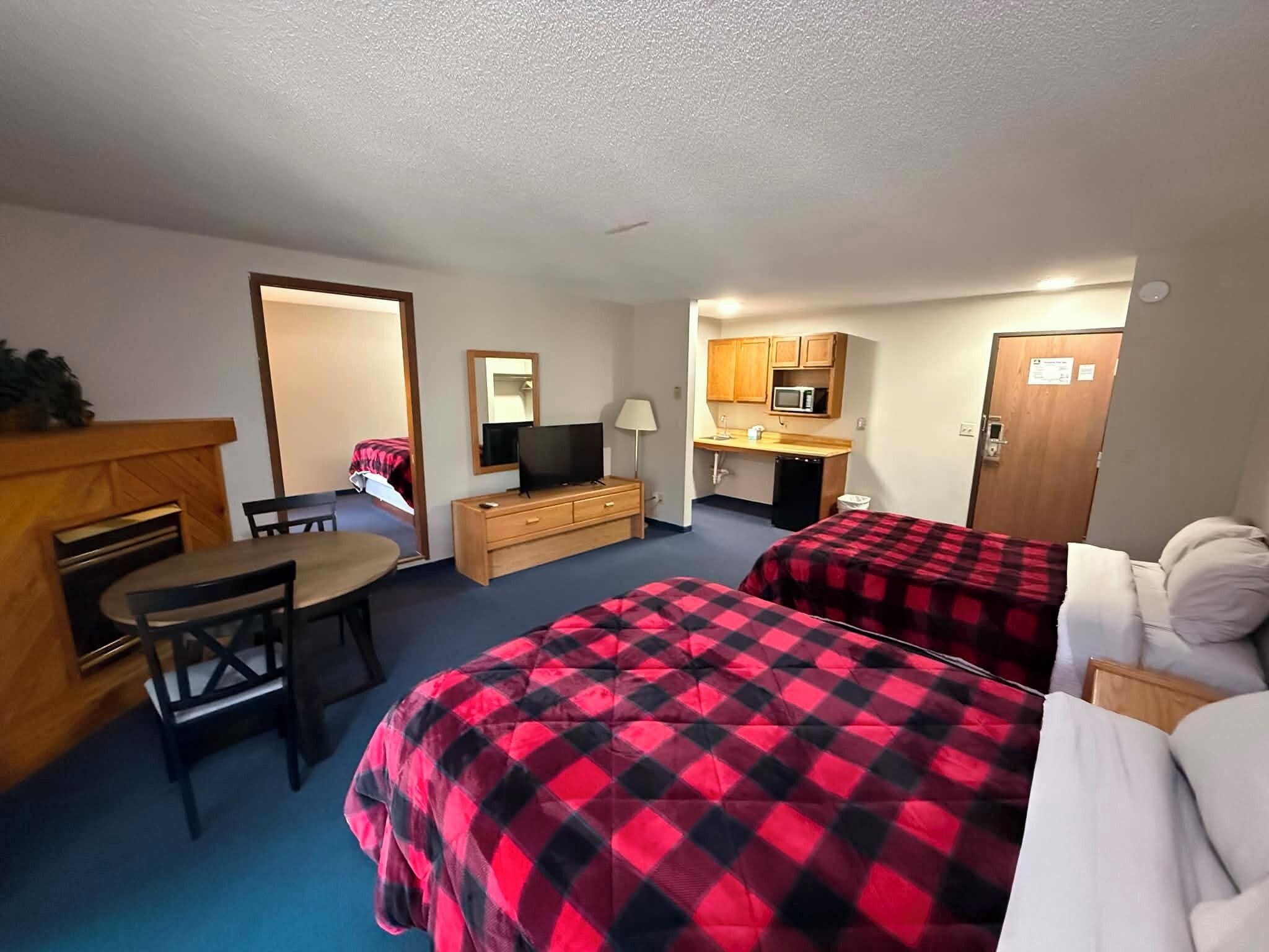 Habitación de hotel con dos camas, un escritorio, televisor, microondas y una pequeña cocina.