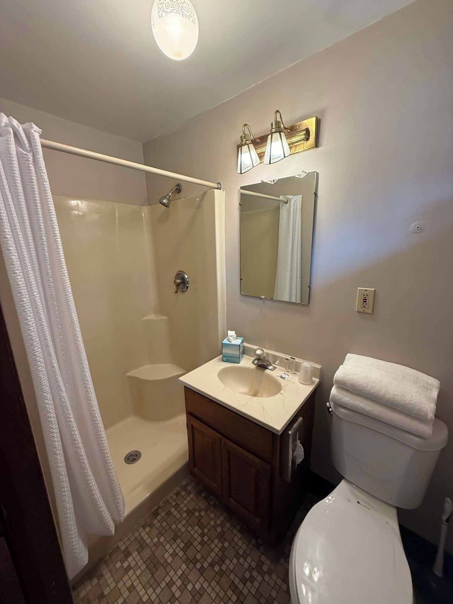 A bathroom with a shower, toilet, sink, and a mirror above the sink.