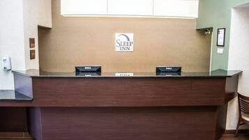 A reception desk at Sleep Inn with a sign above it, a nameplate, and a computer on the desk.