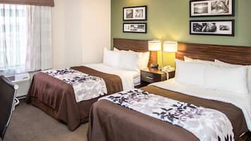 Una habitación de hotel con dos camas, un escritorio, una silla y un ventanal con cortinas.