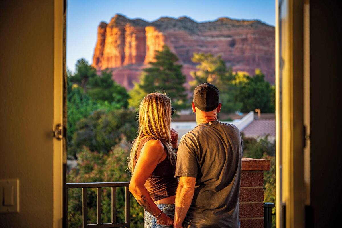 A couple standing on a balcony overlooking a scenic view of red rock formations.