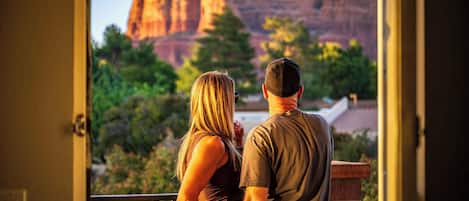 A couple standing on a balcony overlooking a scenic view of red rock formations.