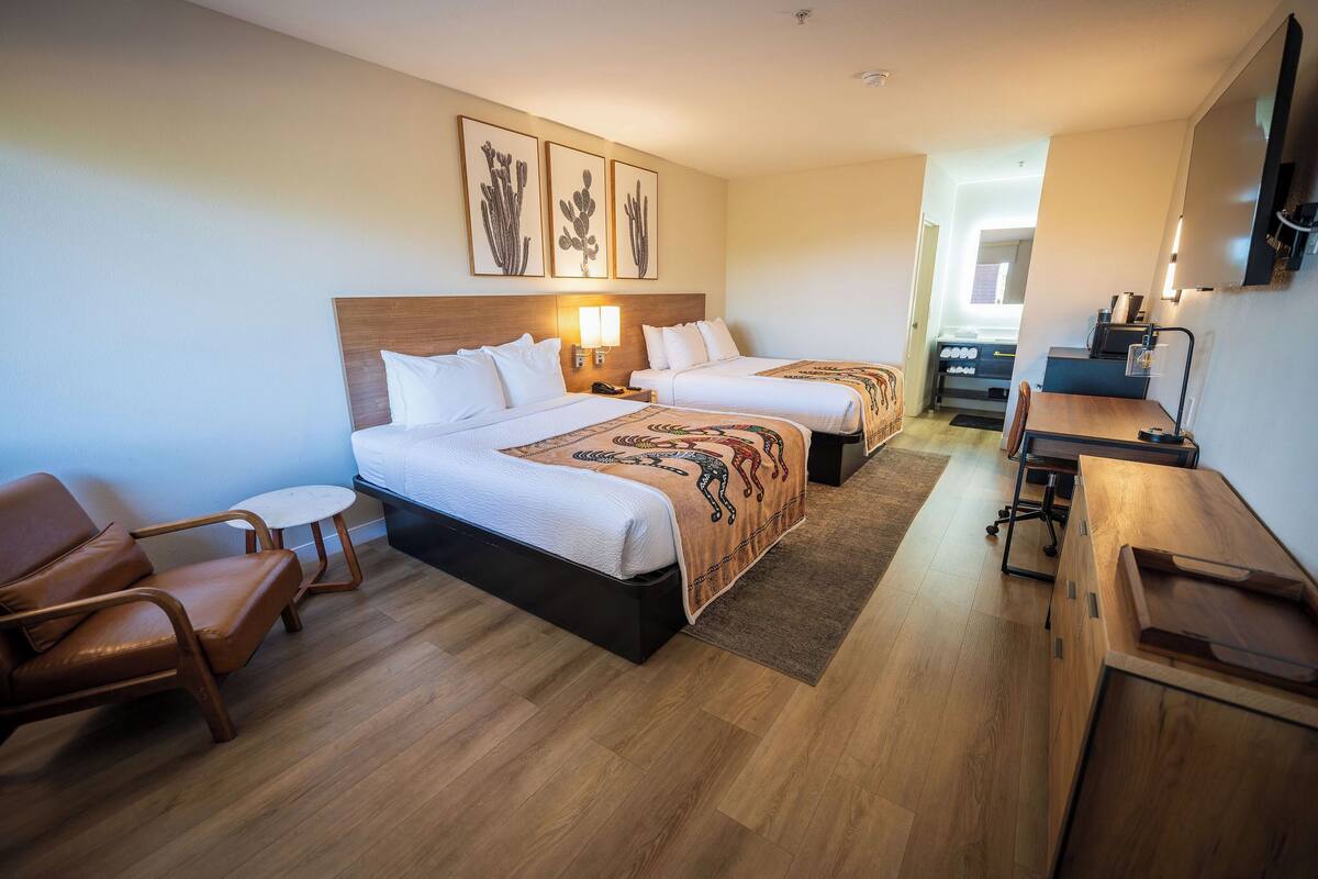 A hotel room with two beds, a desk, a chair, and a small table.