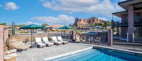 A swimming pool with lounge chairs and umbrellas, a fenced area, and a mountain in the background.