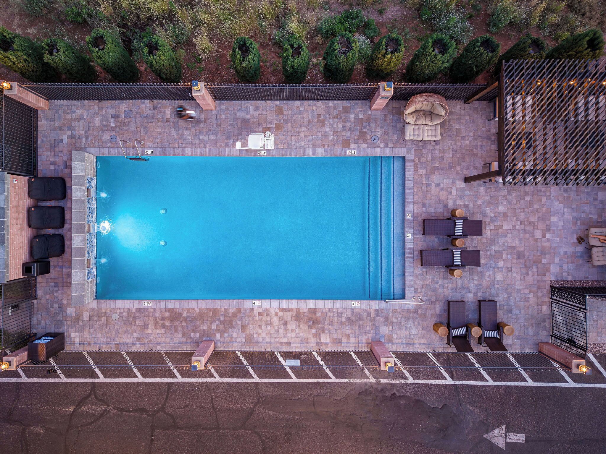 An aerial view of a swimming pool with lounge chairs, a hot tub, and a patio area.