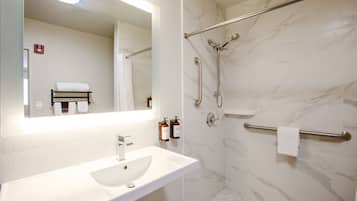 A bathroom with a white sink, mirror, and shower with grab bars.