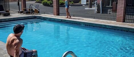 Uma piscina com grades de metal, uma toalha na borda e uma pessoa sentada sobre uma toalha.