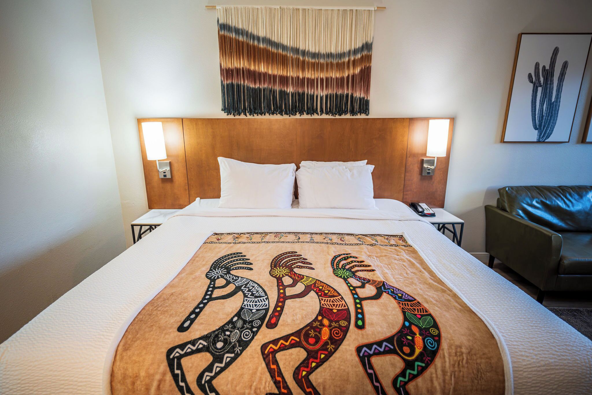 Une chambre d’hôtel avec un lit, deux lampes de chevet, une tapisserie murale et une œuvre d’art encadrée.