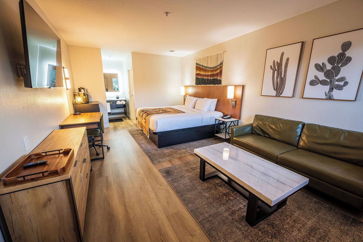 A hotel room with a bed, a desk, a coffee machine, a couch, and two framed wall art pieces.