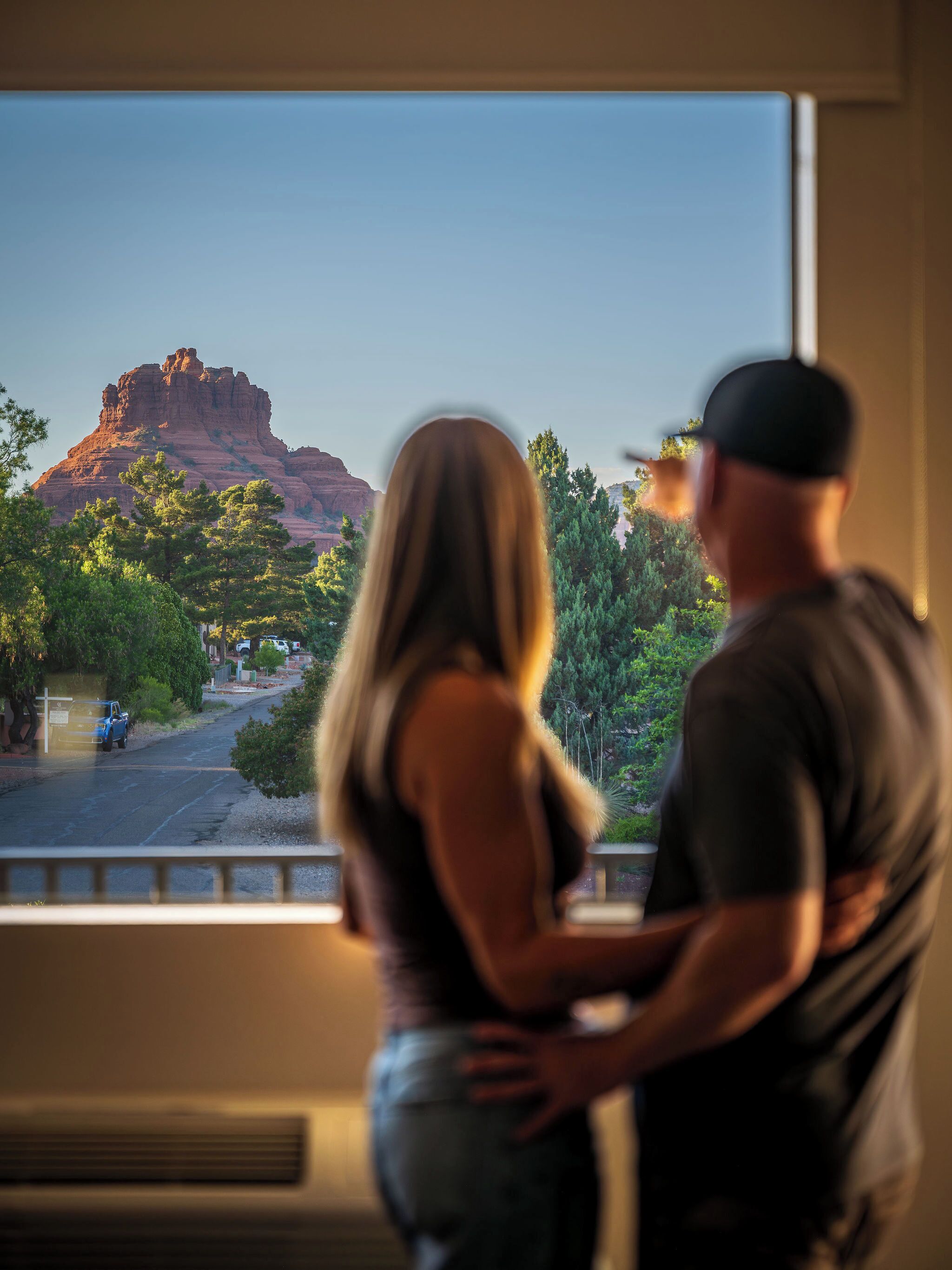 A couple standing in front of a window with a view of a mountain and trees.