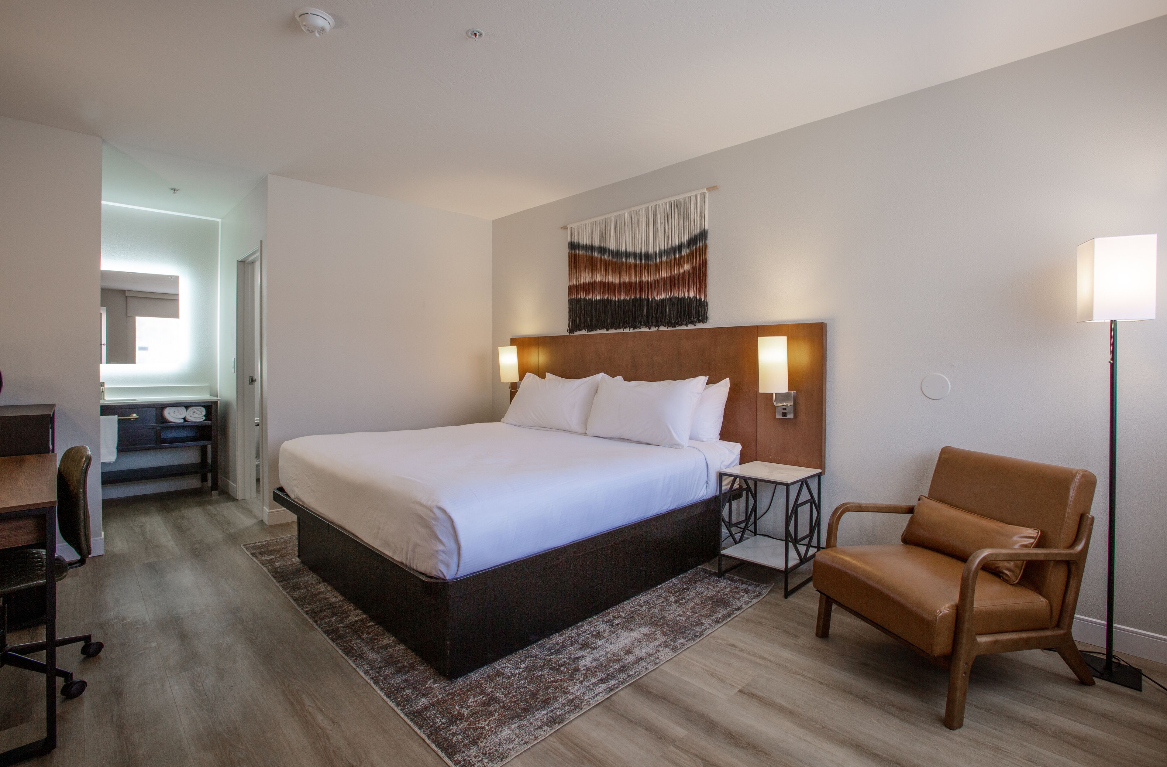 Habitación de hotel con una cama grande, un escritorio, una silla y una lámpara fijada a la pared.
