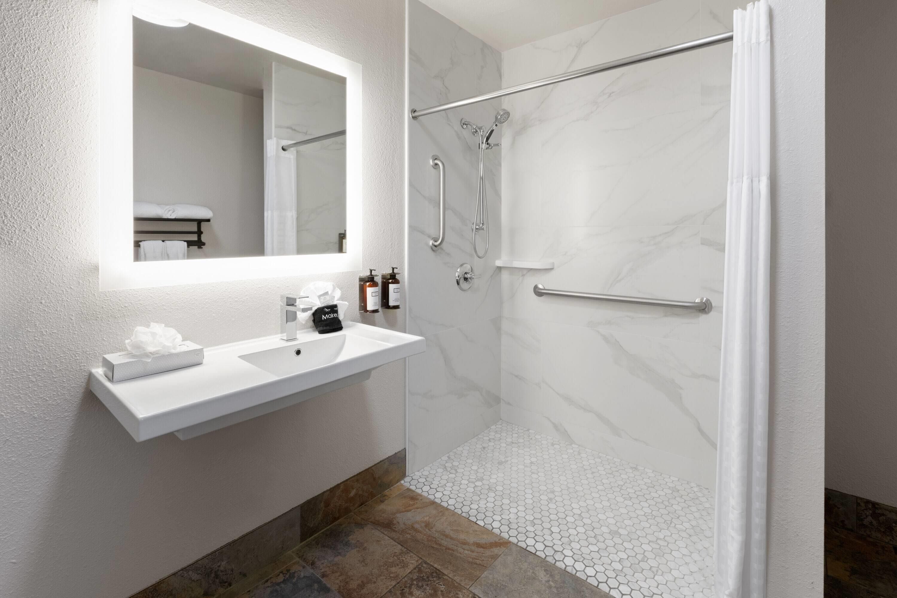 Un baño moderno con un lavamanos blanco, un espejo grande y una ducha con puerta de cristal.