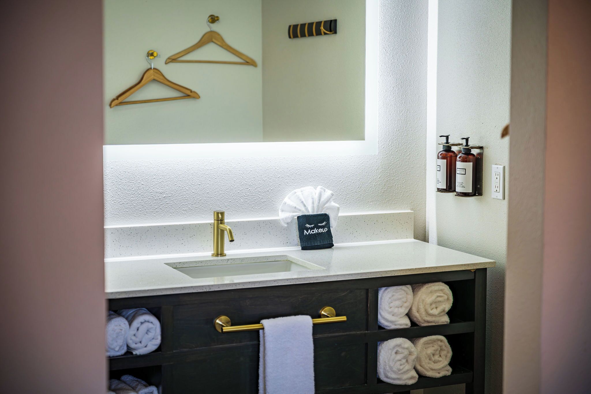 Un baño con lavamanos, toalleros, espejo y neceser.