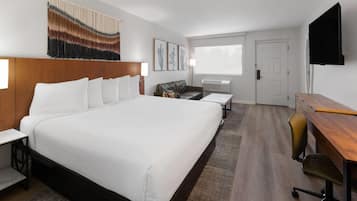 A hotel room with a large bed, a desk, a chair, a sofa, and a TV mounted on the wall.