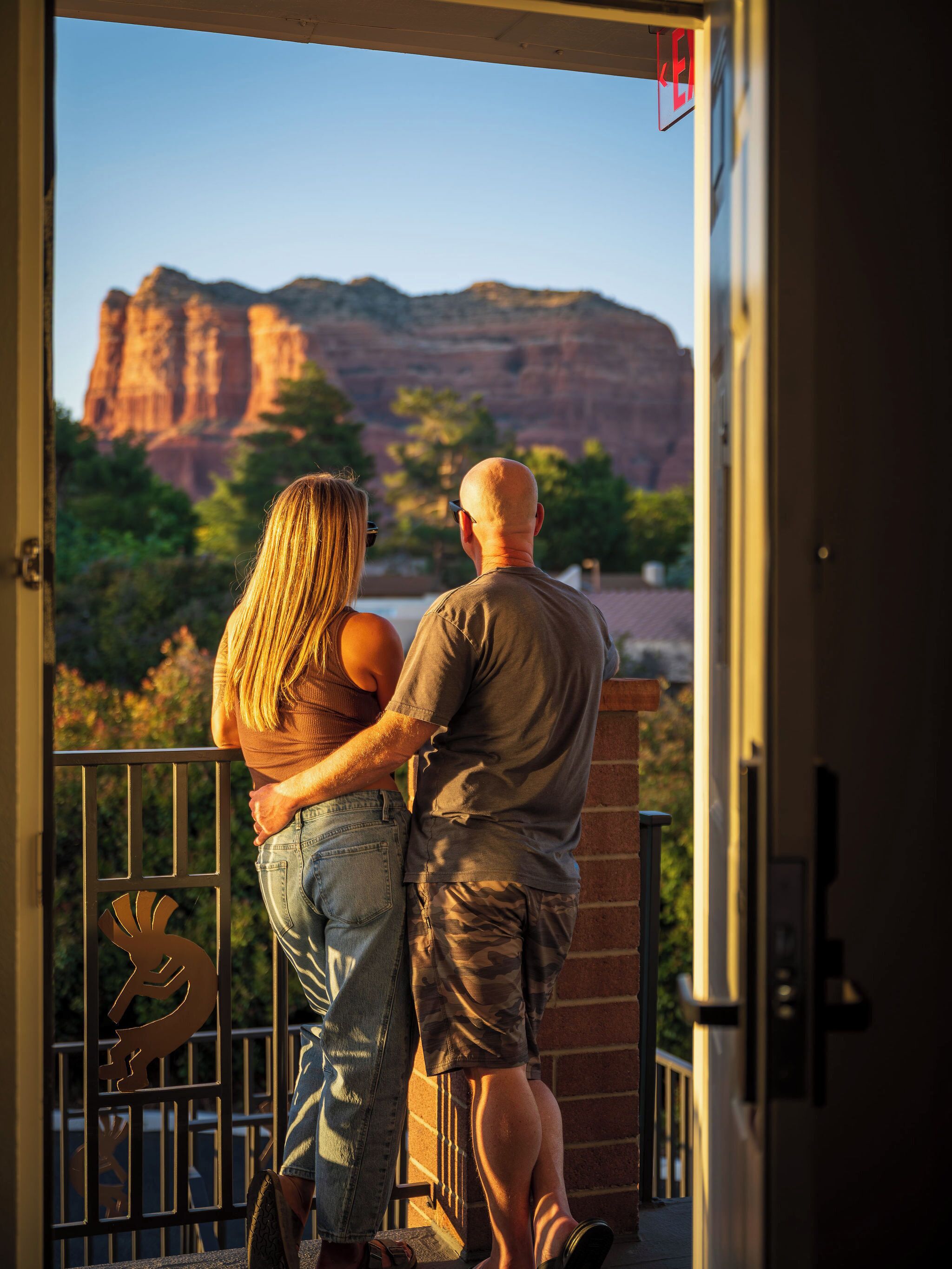 Un couple se tient sur un balcon, d’où l’on peut admirer des formations rocheuses rouges.